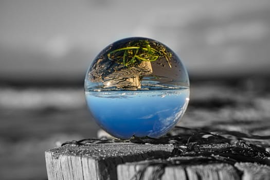 glass globe on the beach of the baltic sea. Black and white photo with a color glass ball