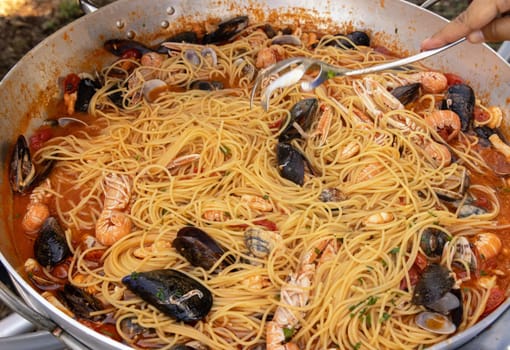Italian spaghetti allo scoglio, pasta with seafood and tomatoes close up in a frying pan. Mediterranean Apulian traditional food with fresh stewed clams, shrimps, mussels, scampi, octopus and squid