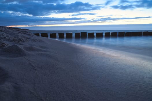 sunset on the beach of the Baltic Sea. Groynes reach into the sea. blue hour with clouds in the sky. Landscape photo in Zingst