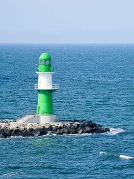 green white lighthouse on the Warnow River in Rostock on the Baltic Sea. Landmark of the city. Waves on the stone edge. Landscape photo from Germany