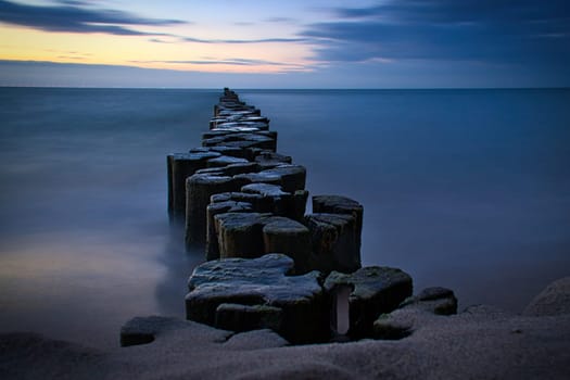 Groynes protruding into the horizon in the Baltic Sea. Long exposure with muted colors. Landscape shot by the sea