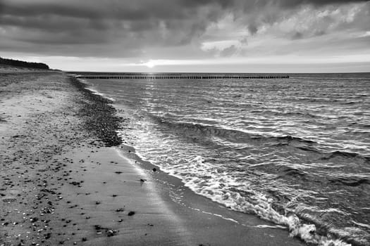 at sunset, a view over the beach in Zingst on the Baltic Sea. Walk along the sea in black and white. Moving clouds in the sky
