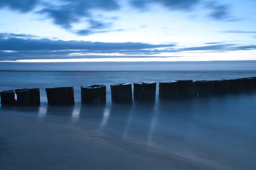sunset on the beach of the Baltic Sea. Groynes reach into the sea. blue hour with clouds in the sky. Landscape photo in Zingst