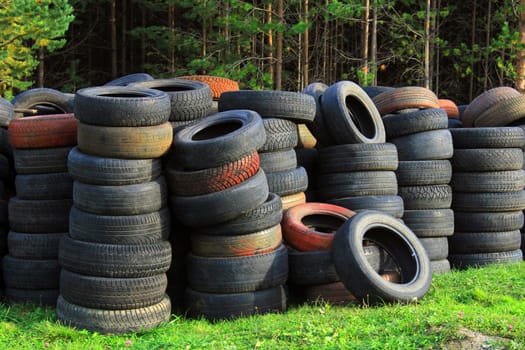A pile of old car tires lies on the grass against the background of the forest. Ecology concept.
