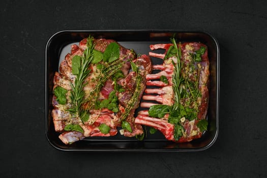 Overhead view of marinated rack of lamb with herbs in baking tray