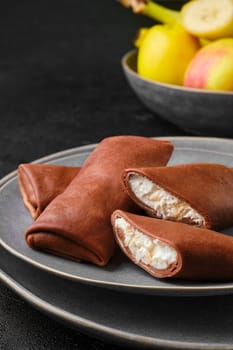 Closeup view of thin chocolate pancakes stuffed with curd, banana and apple