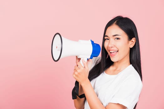 Portrait of happy Asian beautiful young woman teen confident smiling face holding making announcement message shouting screaming in megaphone, studio shot isolated on pink background, with copy space