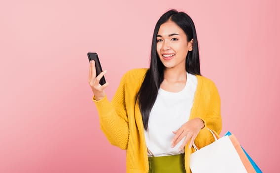 Portrait Asian happy beautiful young woman teen shopper smiling standing excited holding online shopping bags online colorful multicolor and smartphone on hand, studio shot isolated on pink background