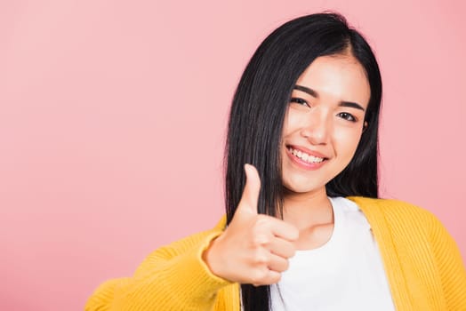 .Portrait Asian beautiful young woman smile she standing made finger thumbs up, Ok sign to agree studio shot isolated on pink background, Thai female successful like finger gesture with copy space