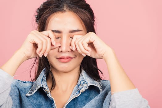Asian portrait beautiful cute young woman wear denim bad mood her cry wipe tears with fingers, studio shot isolated on pink background, Thai female feeling sad unhappy crying with copy space