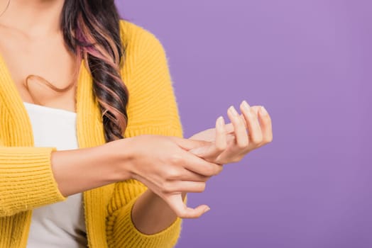 Portrait of Asian beautiful young woman suffering from pain in palm or hands and massaging her painful hands, studio shot isolated on purple background, Health care arthritis concept
