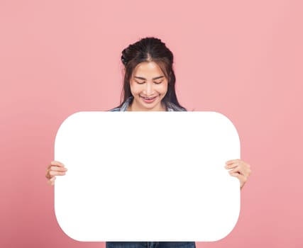 Happy Asian beautiful young woman smiling excited wear denims holding empty speech bubble sign, Portrait female posing show up for your idea looking at bubble, studio shot isolated on pink background