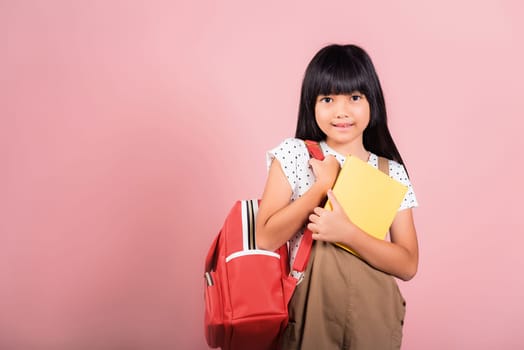 Asian little kid 10 years old with backpack is staying ready for back to school at studio shot isolated on white background, Portrait of happy child girl with school bag and holding or hugging books