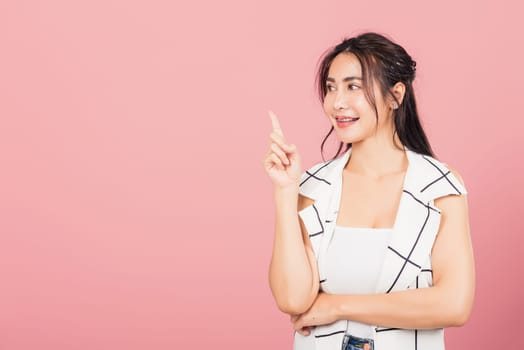 Happy Asian portrait beautiful cute young woman standing smiling indicate finger empty space looking to space, studio shot isolated on pink background, Thai female pointing index out with copy space
