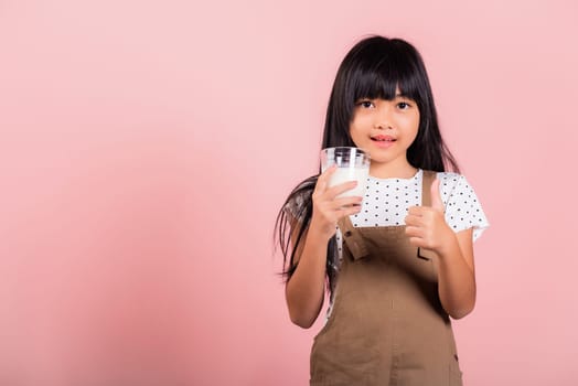 Asian little kid 10 years old smile hold milk glass drink white milk and show thumb up finger for good sign at studio shot isolated on pink background, Happy child girl daily health care medicine food