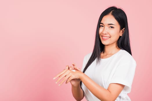 Portrait of Asian beautiful young woman applying lotion cosmetic moisturizer cream on her behind the palm skin back hand, studio shot isolated on pink background,  Hygiene skin body care concept