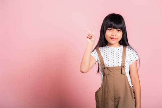 Asian little kid 10 years old show v-sign fingers gesture at studio shot isolated on pink background, Happy child girl lifestyle making victory symbol sign