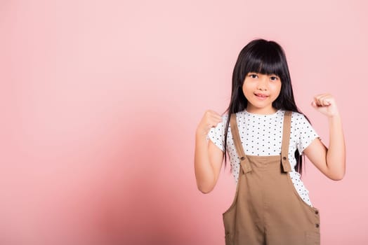 Yes ! Asian little kid 10 years old celebrating great success with arms raised at studio shot isolated on pink background, Happy and excited child girl positive smiling cheerful