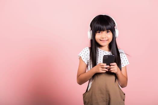 Asian kid 10 years enjoying listening music from mobile phone wear wireless headset at studio shot isolated on pink background, Happy child girl lifestyle use smartphone listen music with headphones