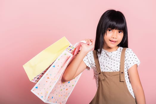 Asian little kid 10 years old smiling holding multicolor shopping bags in hands at studio shot isolated on pink background, Portrait of Happy child girl shopper lifestyle, Black friday concept