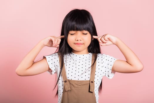 Asian little kid 10 years old Close her ears with fingers and eyes at studio shot isolated on pink background, child girl does not want to listen, Stress and noise concept