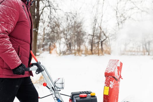 Detail of portable red snow blower powered by gasoline in action. Man outdoor using snowblower machine after snowstorm. Snow removal, thrower assistant in winter. Guy blowing snow during blizzard