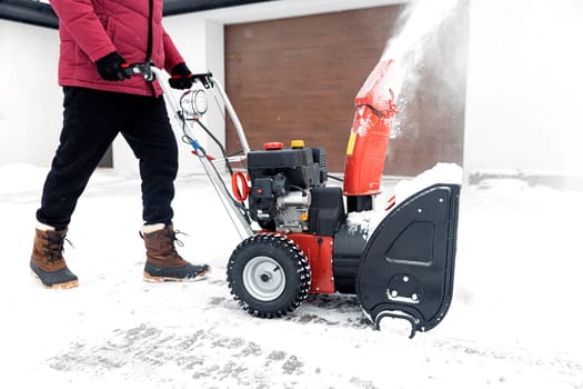 Detail closeup of portable red snow blower powered by gasoline in action. Senior mature man outdoor in front of house using snowblower machine after snowstorm, snowfall for clearing, removing snow