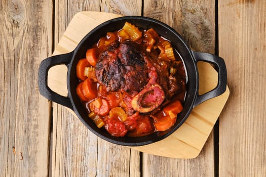 Overhead view of cast iron skillet with ossobuco on wooden table