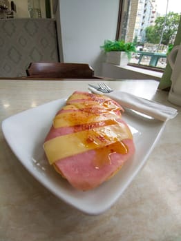 Ham toast with sliced cheese sprinkled with Pimenton de la Vera. Knife and fork wrapped in a paper napkin