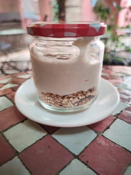 Closed Jar full of yogurt with muesli at the bottom over glazed tile mosaic table. Mediterranean style background