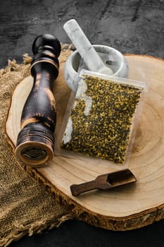 Wooden cross section with lemon pepper in plastic package and stone mortar and mill