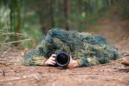 Photographer wearing camouflage clothing in the forest, wildlife animal photography with a camera and telephoto lens