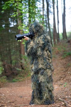 Photographer wearing camouflage clothing in the forest, wildlife animal photography with a camera and telephoto lens