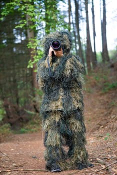 Photographer wearing camouflage clothing in the forest, wildlife animal photography with a camera and telephoto lens