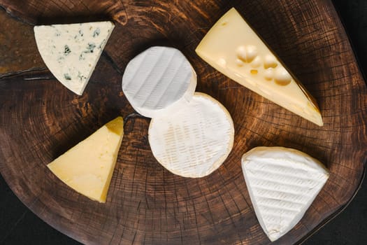Top view of cheese platter. Assortment of brie, camembert, parmesan and gouda cheese on wooden cutting board.