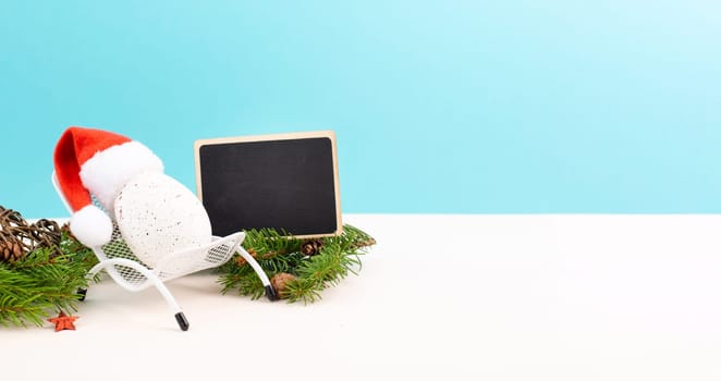 Santa Claus with a red hat sitting in a lounge chair, holiday by the sea, taking a vacation, christmas decoration with fir, cones and stars