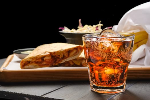 Glass of cola with ice with tortilla and fried potato on background (focus on foreground)