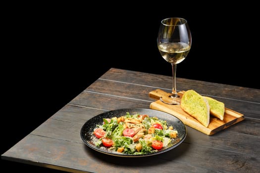 Salad with chicken fillet, tomato and cheese with glass of white wine on a table