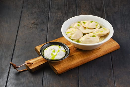 Bowl with beef pelmeni with sour cream on a wooden serving board