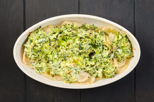 Overhead view of meat dumplings with spinach and cheese sauce baked in oven