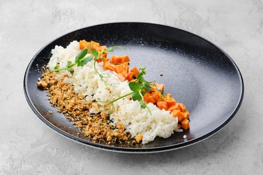 Garnish to the main dish - boiled rice, fried carrot and bread crumbs on a plate