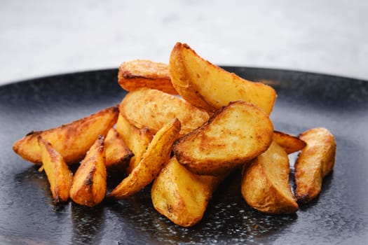 Garnish to the main dish - Slices of potato wedges fried in oil, closeup view