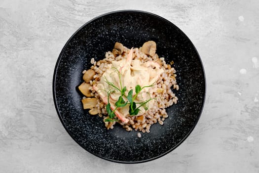 Boilet pearl barley with fried mushrooms and creamy flour sauce on a plate, top view