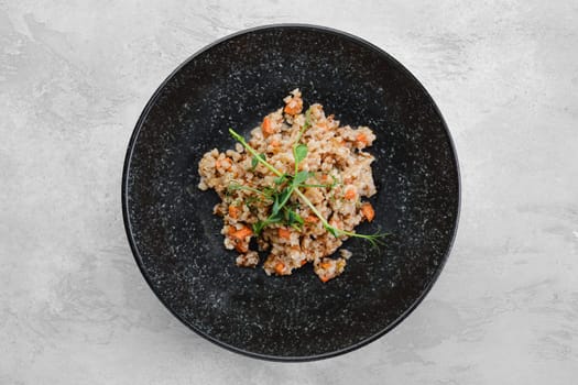 Garnish to the main dish - buckwheat porridge with slices of fried carrot on a plate, top view