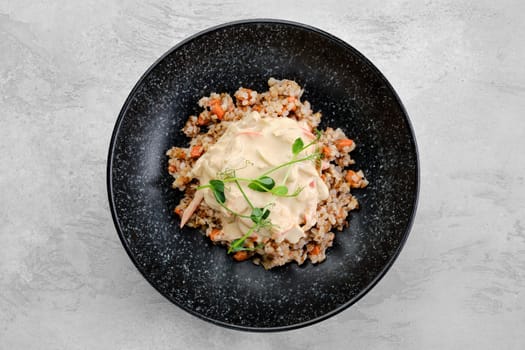 Buckwheat porridge with slices of fried carrot and creamy flour sauce on a plate, top view