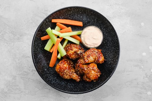 Fried chicken legs with teriyaki sauce and slices of celery and carrot on a plate, top view