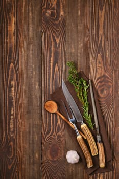 Steak fork, knife and sharpener on napkin over brown wooden background