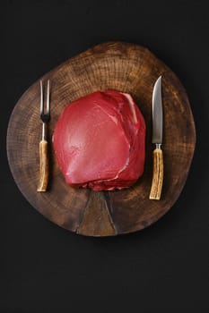Raw beef top round meat, whole uncut section on wooden slab