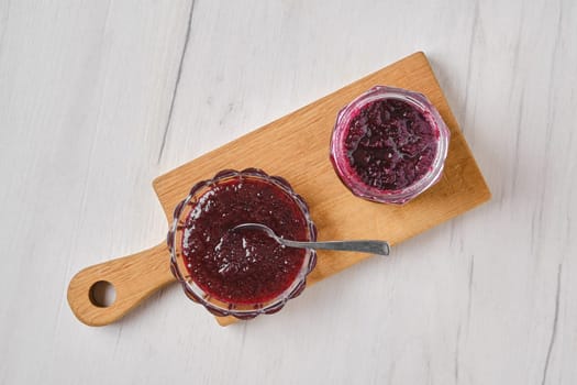Overhead view of homemade blueberry jam in a jar and saucer on wooden serving board