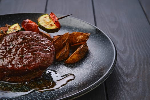 Closeup view of juicy beef steak with potato wedges and grilled vegetables on skewer